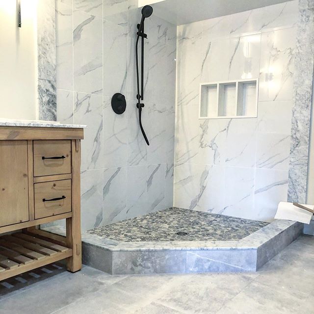 Custom marble-look shower with pebble floor, three niches, and matte black fixtures