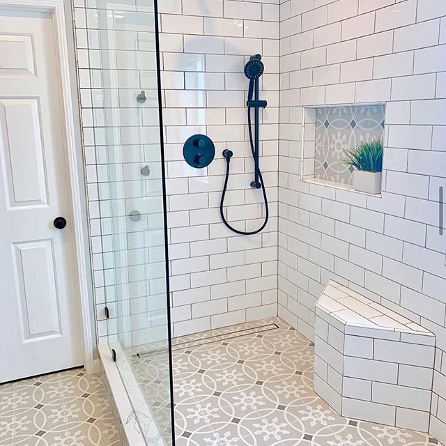 White subway tile shower with patterned floor, built-in bench, niche, and black fixtures